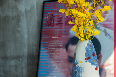 Bouquet of flowers in Purple ceramic vase on white textured table cloth in front of Classic chinese poster movie frame with old cement wall. Home decor, Selective focus.の写真素材