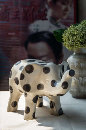 Bangkok, Thailand -Feb 06, 2021 :  Elephants shaped ceramic and Bouquet of flowers in ceramic vase on white textured table cloth in front of Classic chinese poster movie frame. Home decor, No focus, specifically.の写真素材