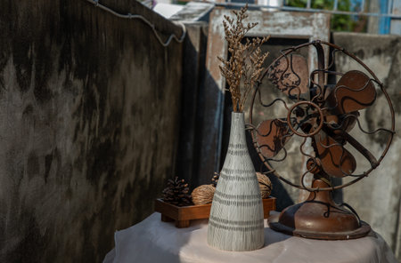 Dried flowers in Two ceramic vase on pink textured table cloth and vintage fan with Old cement wall....