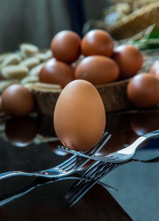 Fresh chicken egg (Hen egg) balanced on a composition of two intertwined forks with fresh chicken eggs on wood background. Selective focus.の写真素材