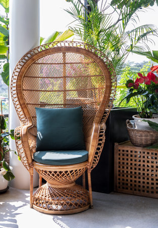 Peacock wicker rattan chair and flowers in living room overlooking the garden. Wicker chair interior...