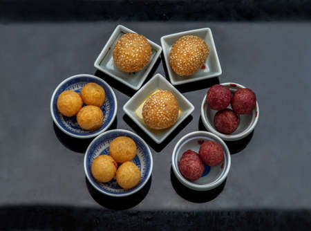Fried Sweet Potato Balls with sesame with Deep fried purple and yellow sweet potato balls (Quail candy eggs) on black table. Thai Traditional dessert snack made from cassava flour (tapioca starch) and sweet potato, Selective focus.の写真素材