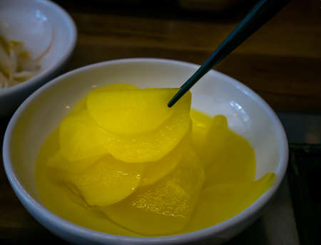 Hand using chopsticks pick Korean seasoned beansprout (Mild kongnamul muchim) in a white cup for eating. Asian side dish Pickled radish, Korean food traditional. No focus, specifically.の写真素材