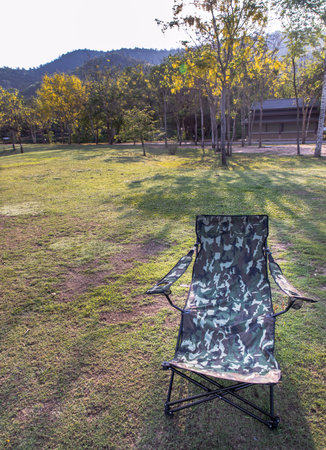 Empty camouflage color portable folding camping chair at the nature park on a warm sunny day in the...