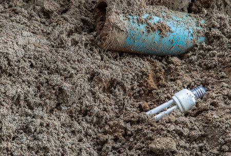 The remains of burnt energy-saving lamp are left on the beach sand. Hazardous and toxic electronic...