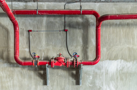 Red water or gas pipeline with gate pressure valve on concrete wall. Industrial tubes and valves,...