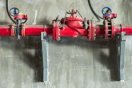 Red water or gas pipeline with gate pressure valve on concrete wall. Industrial tubes and valves, Line pipe industrial and extinguisher pump, Copy space, Selective focus.の写真素材
