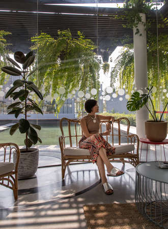 A young asian woman sitting and relax on cushion on rattan sofa  near glass window in living room. Selective focus.の写真素材
