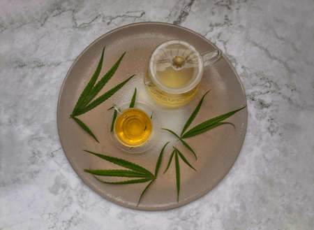 Refreshing and enjoy with A cup of Cannabis herbal tea and Stem with green marijuana leaves on marble table for medical purposes for sleep and anxiety. Herbal tea and healthy drinks concept. Top view, Selective focus.の写真素材