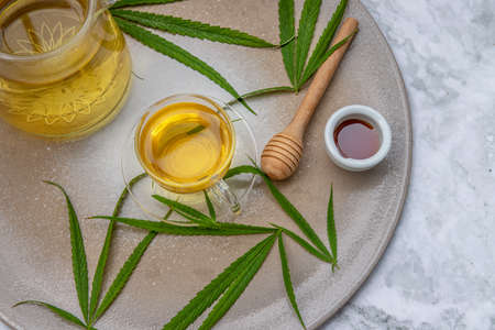 Refreshing and enjoy with A cup of Cannabis herbal tea and Stem with green marijuana leaves with honey on marble table for medical purposes for sleep and anxiety. Herbal tea and healthy drinks concept. Copy space, Selective focus.の写真素材