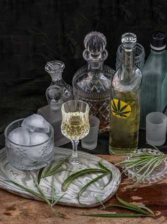 Ice cold Marijuana cannabis CBD infused drink in a crystal clear glass with green marijuana leaf on wooden background. Cannabis cocktail, Medical purposes for sleep and anxiety, Herbal and healthy drinks concept. Selective Focus.の写真素材