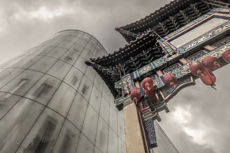 London, England - 15 Mar 2019 : Contrast of modern glass building with Chinatown entrance gate in traditional chinese design. Selective focus.のeditorial素材