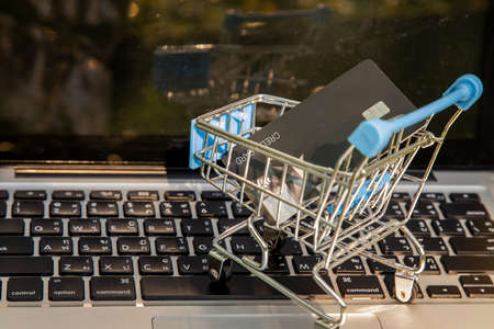 A credit card in a Mini supermarket trolley on a laptop keyboard. E-commerce and online shopping concept. Ideas about home shopping or buying things in virtual malls / stores from home or office by using modern technology called internet and web browser.の写真素材