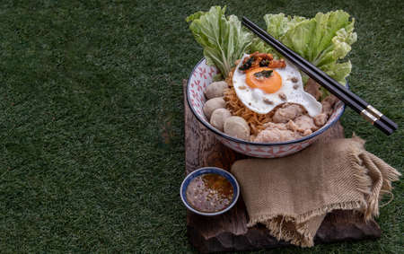 Egg noodles soup with pork ball, minced pork, fried egg, vegetables and soups in bowl and chopstick with spoon and timber background. Thai noodle soup.の写真素材
