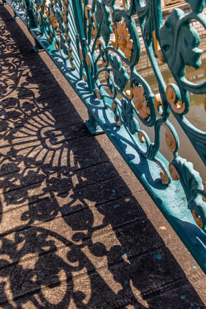 Wrought iron decorative fence on bridge. Forming an interesting design with it's cast shadow on the floor. Selective focus.の写真素材