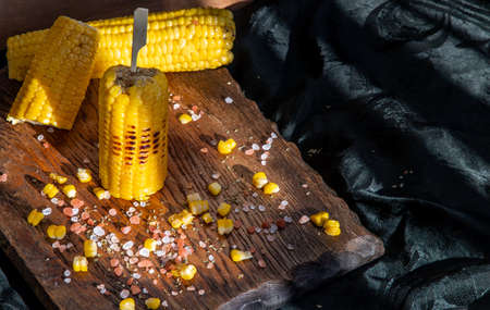 Grilled corn on the cob  on rustic wooden board   over dark background. Ideas for barbecue and grill parties, Barbecue concept.の写真素材