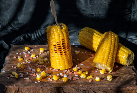 Grilled corn on the cob  on rustic wooden board   over dark background. Ideas for barbecue and grill...