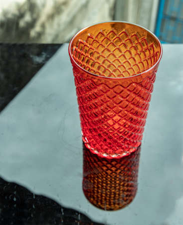 Colored transparent red glass cup for water drinking and surface reflections on a black background. Copy space, Selective focus.の写真素材