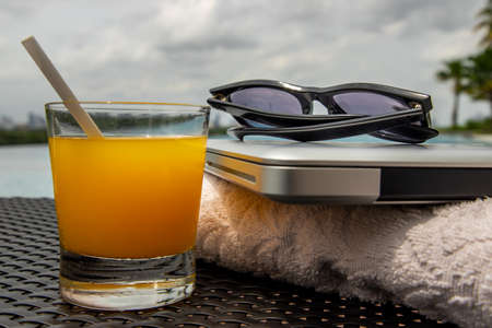 Relaxing moment by the pool. Take a break from working on laptop and enjoy the fresh orange juice for a refreshment.  Outdoor swimming pool background. leisure activity.の写真素材