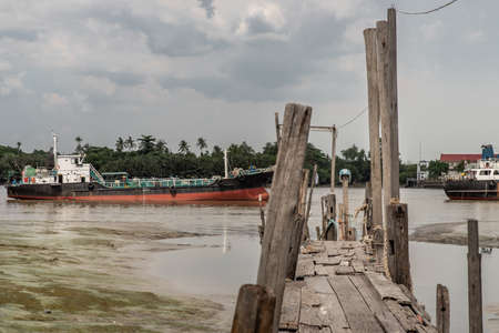 Bangkok, Thailand - 10 Jul 2020 : The old broken wooden pier by Chao Phraya River with cargo ship at the background.のeditorial素材