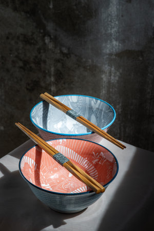 Two ceramics bowls with wooden chopsticks on pink table cloth. Ceramic tableware, Beautiful...