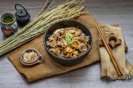 Japanese pork rice bowl with egg and onion (Donburi) served with pickled ginger and green tea on wooden table. Japanese food style.の写真素材