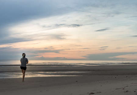 Young woman exercising on the sea beach at sunrise. Back view, Copy space, Selective focus.の写真素材