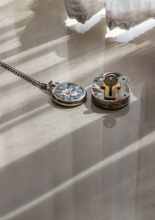 A retro pocket watch and Old vintage iron padlock is placed on the floor of the room that have early light through the beautiful curtain for background. Concept of light, hope and Value of time. Copy space, Selective focus.の写真素材