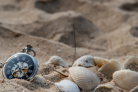 Antique pocket watch and shells in sand on the beach and copy space. Time of life in nature concept. Selective focus.の写真素材