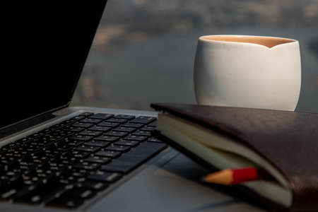 Workplace area with laptop, fruit juice mug and notebook with pencil Comfortable office work table and blurry city view. Selective focus.の写真素材