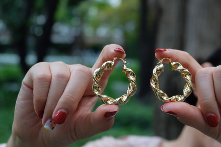 Golden earrings on women hands and red nail on garden background. Women accessories. Selective...