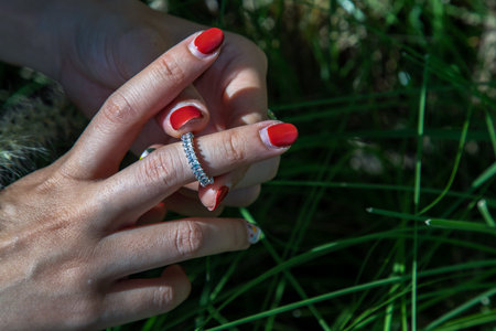 Women hand. Sterling silver female ring on the fingers of a lady and red nail on nature background....