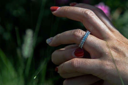 Women hand. Sterling silver female ring on the fingers of a lady and red nail on nature background. Beauty and accessories, No focus, specifically.の写真素材