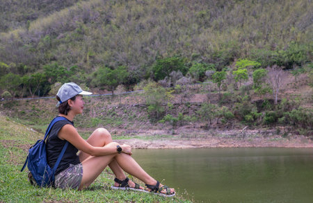 Side view of a young asia woman sitting and enjoying peaceful moment of beautiful view at lake shore...