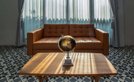 Chiang Rai,Thailand - Sep 06, 2020 : Replica globe on wooden coffee table front to brown leather sofa on background of white curtains and glass windows in living room with copy space. Selective focus.のeditorial素材