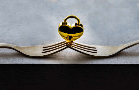 Golden heart shaped love padlock balanced on a composition of two intertwined gold forks. Valentine's day concept, Copy space, No focus, specifically.の写真素材