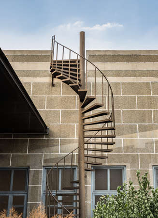 Brown metal spiral staircase with iron railing lead down from Rooftop balcony to the first floor in front of brick textured wall. Selective focus.の写真素材