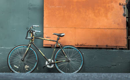 One bicycle in front of steel orange door with green wall of warehouse. Copy space, Selective focus.の写真素材