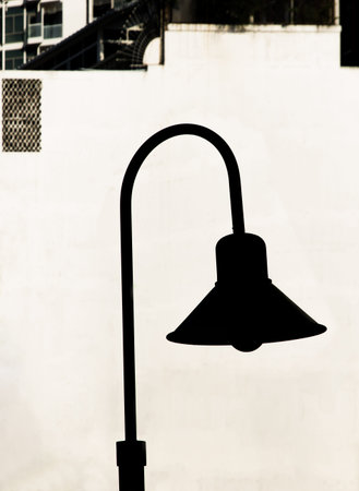 Shadow of Street lamp and a steel pole on surface white concrete wall in building in vertical frame. Space for text, Selective focus.の写真素材