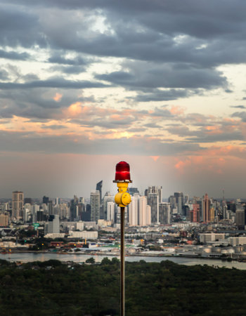 Red lantern of obstruction lights mounted on the rooftop of high rise tall building to ensure...