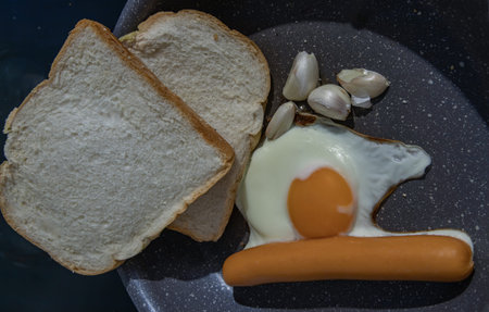 Preparing Breakfast in Cooking pan with Fried egg, Fried sausages Garlic and Two breads. Space for...