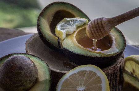 Close-up of Honey dripping from wooden stick dripper into on Fresh organic avocado sliced in half...