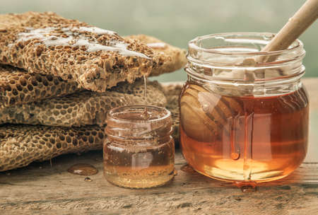 Close-up of Delicious honey dripping from Fresh honeycombs on Glass jar with Wooden honey dipper stick on old wooden table. Healthy organic natura honey, space for text, Selective focus.の写真素材