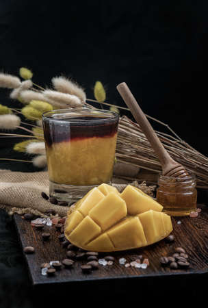 Glass of Iced tropical Mango smoothie mixed Espresso coffee served with Honey on the Wooden cutting board and Dark background. Alternative summer drink for living life, Selective focus.の写真素材