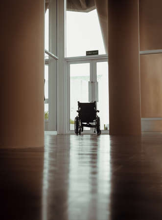 The back of an empty wheelchair with no one sitting as if looking outside through a glass door. Near the exit glass door with a blurred outside view of the garden in background. There is always hope in life, Copy space, Selective focus.の写真素材