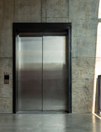 Elevator chrome metal with closed door on Bare cement wall for lifting people to the upper floors with push switch for up and down at modern building design. Selective focus.の写真素材