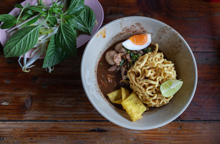 Crispy fried yellow egg noodles in thicken soup added blood with Pork balls, Sliced pork, Sliced bael eggs, Sliced lime and Crispy wonton (Nam tok egg noodles) Serve with basil and bean sprouts. Thai Boat noodles soup or Guay tiew reua is Thailand's most famous noodles soup, Top view, Selective Focus.の写真素材