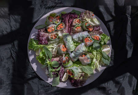 Healthy vietnamese spring rolls with fresh vegetables and lime slices on round ceramic tray and dark background. Top view, Selective focus.の写真素材