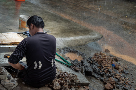 Bangkok, Thailand - Jun 27, 2022 : Utility worker using tool to fixing broken water main for commercial building water supplies during a rain. Plumbing problems. Selective focus.のeditorial素材