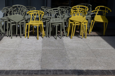 Stack of Dark green (Khaki color) and Yellow plastic chairs are beside of The cafe terrace at sunny day. Space for text, Selective focus.の写真素材